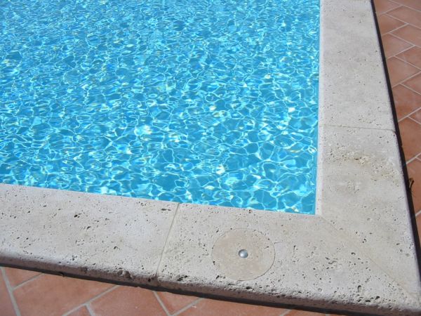 Angolo di una piscina con bordo in pietra.