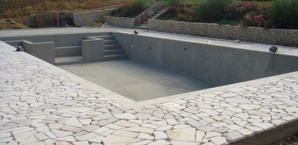 Piscina vuota in costruzione con bordo in pietra.