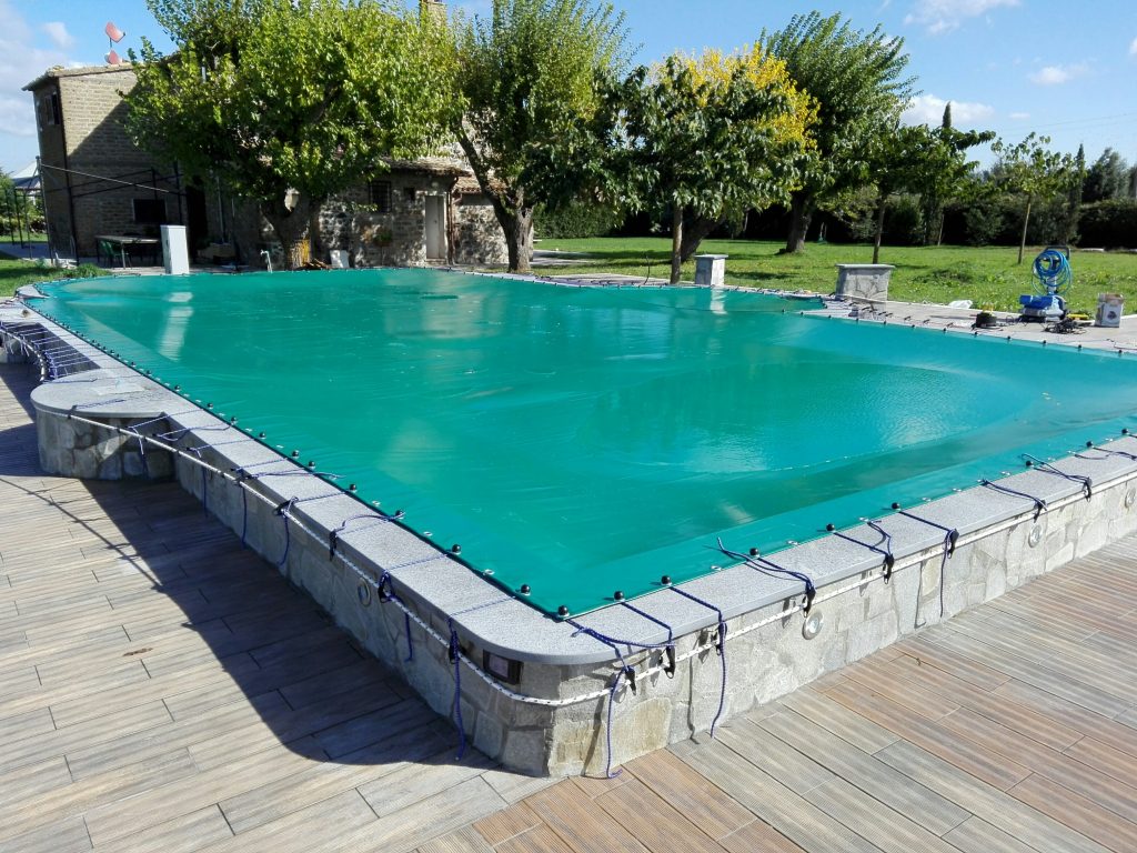 Piscina coperta con telo verde, circondata da alberi.