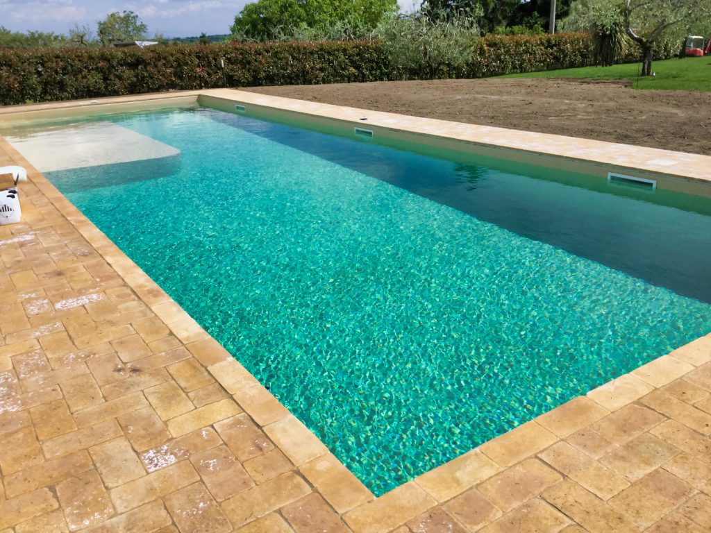 Piscina rettangolare con bordo in pietra, giardino circostante.