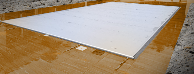 Copertura bianca su piscina vuota con pavimento bagnato.