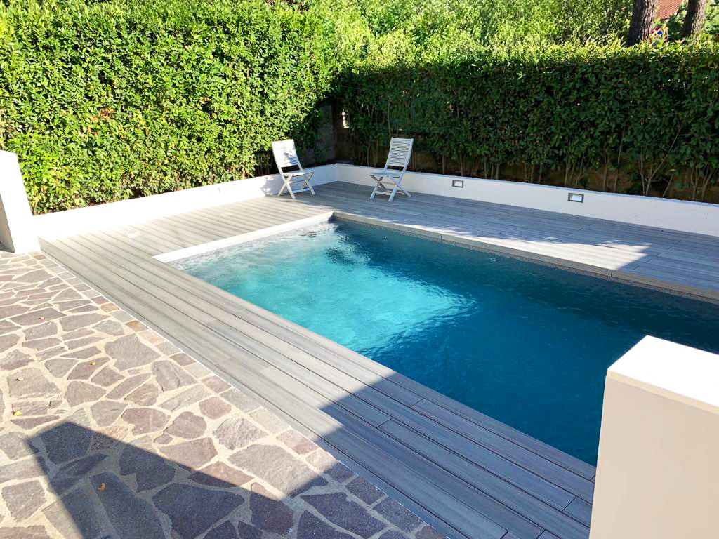 Piscina con sedie bianche e siepe verde.